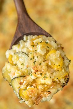 a wooden spoon filled with food on top of a casserole covered in cheese