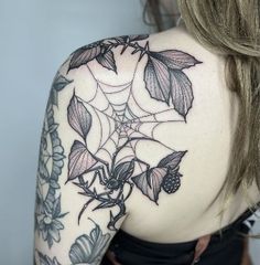 the back of a woman's shoulder with leaves and spider web tattoo on it