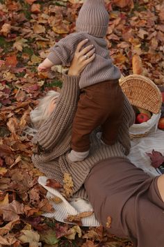 a woman holding a baby in her arms while laying on leaves with apples and hotdogs