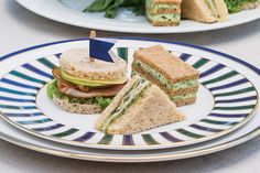 two plates with sandwiches cut in half on top of each other and green leaves behind them