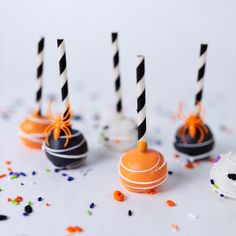 four halloween cake pops with black and white striped straws on them, surrounded by sprinkles