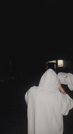 a person wearing a white hoodie is standing in the dark and pointing at something