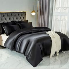 a bed with black sheets and pillows in a white room next to a large window