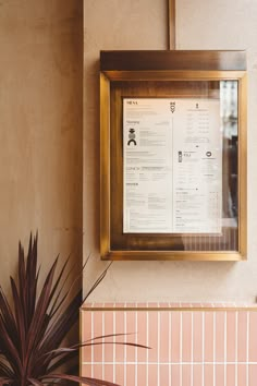 a menu hangs on the wall next to a potted plant