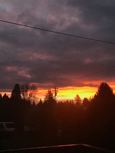 the sun is setting over some trees and power lines in front of a cloudy sky