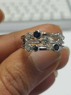 a person is holding two rings with diamonds and sapphires on them in front of a keyboard