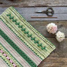 a crocheted blanket with flowers and scissors next to it on a wooden surface