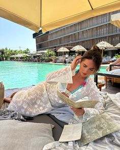 a woman laying on top of a bed next to a pool with an open umbrella