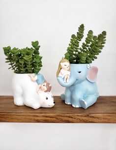 two ceramic elephants with plants in them sitting on a wooden shelf next to each other