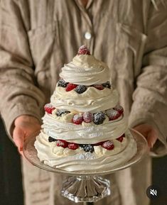 a man holding a cake on top of a glass plate with strawberries and raspberries