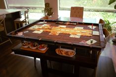 a wooden table topped with plates and bowls filled with food next to a large window