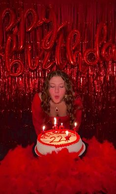 a woman sitting in front of a cake with lit candles on it and red feathers around her