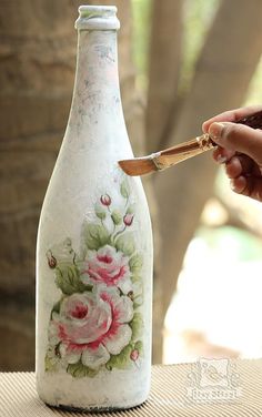 a hand holding a knife near a painted glass bottle with flowers on the outside and inside