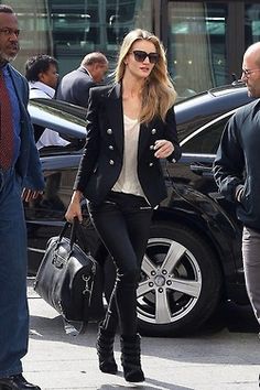 a woman in black pants and jacket walking down the street