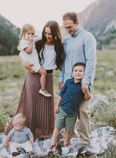 a family is posing for a photo on a blanket in the grass with mountains behind them