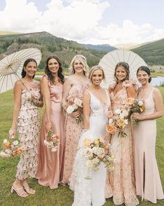 a group of women standing next to each other in front of an open field holding umbrellas