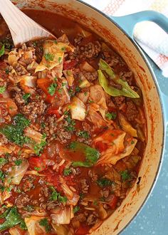 a pot filled with meat and vegetables on top of a blue table cloth next to a wooden spoon