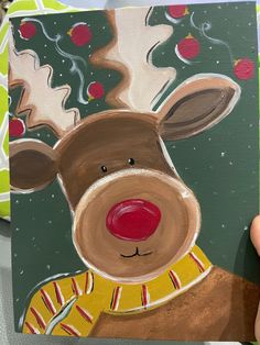 a hand holding up a painting of a reindeer wearing a yellow sweater and red nose