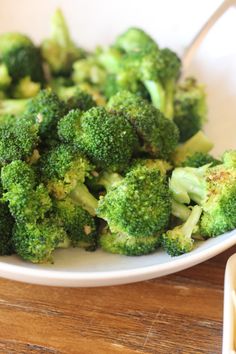 a white plate topped with broccoli on top of a wooden table next to a fork