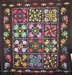 a quilt is hanging on the wall in front of a wooden frame with flowers and leaves painted on it