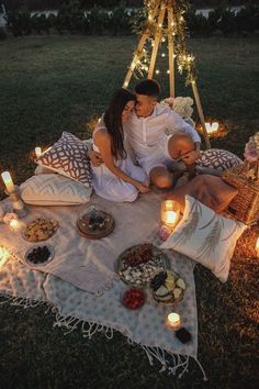 a man and woman are sitting on a blanket in the grass with candles around them