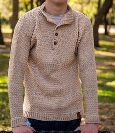 a young man standing next to a bike in a park wearing a sweater and jeans