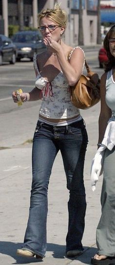 two women are walking down the street and one is holding her hand up to her mouth