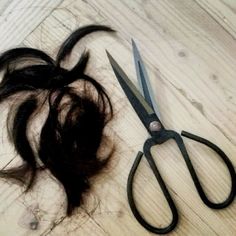 a pair of scissors sitting next to a pile of hair on top of a wooden floor