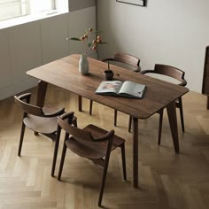 a wooden table with four chairs and a book on it in front of a window