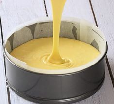 a yellow sauce being poured into a metal pot on a white wooden table with a spoon in it