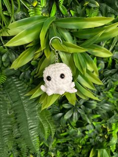 a small white stuffed animal hanging from a green leafy plant with eyes drawn on it