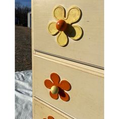 the drawers are painted yellow and orange with flower knobs on each drawer, along with an egg