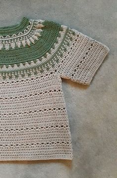 a crocheted sweater with green and white trim sitting on top of a table