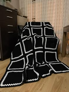 a black and white knitted blanket sitting on top of a wooden floor next to a window