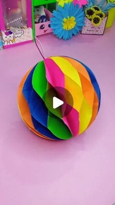 an origami ball on a pink table with flowers in the background and a video playing about how to make it