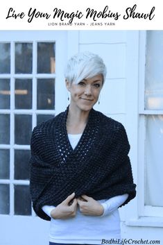 a woman standing in front of a window with her arms crossed, wearing a black knitted shawl