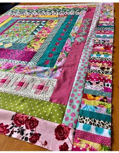 a colorful quilt is laying on a wooden table with polka dots and pink flowers in the center