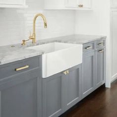 a kitchen with gray cabinets and white marble counter tops, gold faucets and brass pulls