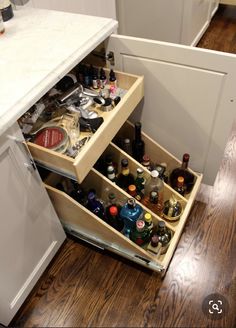 an open drawer in the middle of a kitchen filled with bottles and liquor on top of wooden flooring