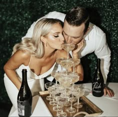 a man and woman kissing in front of champagne glasses on a table with wine bottles