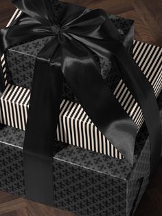 three wrapped gift boxes with black ribbons on them sitting on a wooden floor next to each other