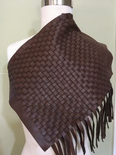 a white mannequin torso wearing a brown woven shawl with tassels