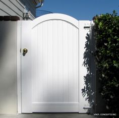 a white gate is open in front of a house with a green bush behind it