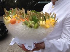 a man holding a bowl filled with fruit and veggies on skewers