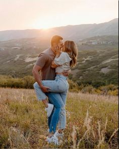 a man and woman kissing in the middle of a field with mountains in the background