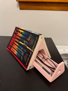 a pair of scissors in a pink box on a black table next to a fan