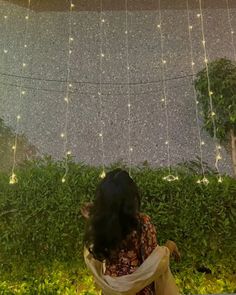 a woman standing in front of a wall covered with lights and greenery at night