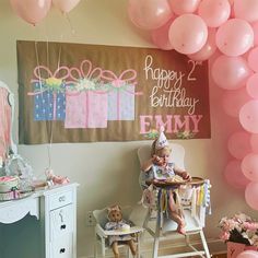 a baby in a high chair with pink balloons on the wall and a happy birthday sign above it