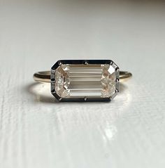 an emerald cut diamond sits on top of a white surface with a thin band around it