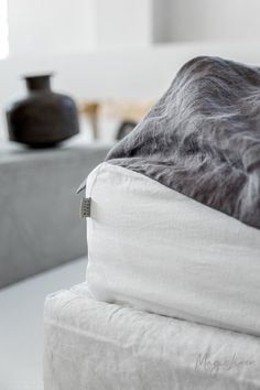 a bed with white sheets and black vases on the table in the back ground